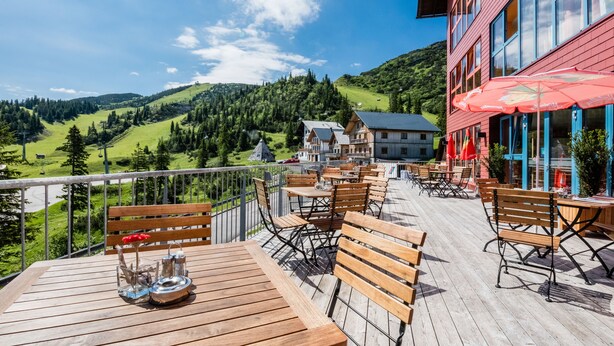 Una terraza de madera con mesas y sillas, con vistas a un paisaje montañoso.
