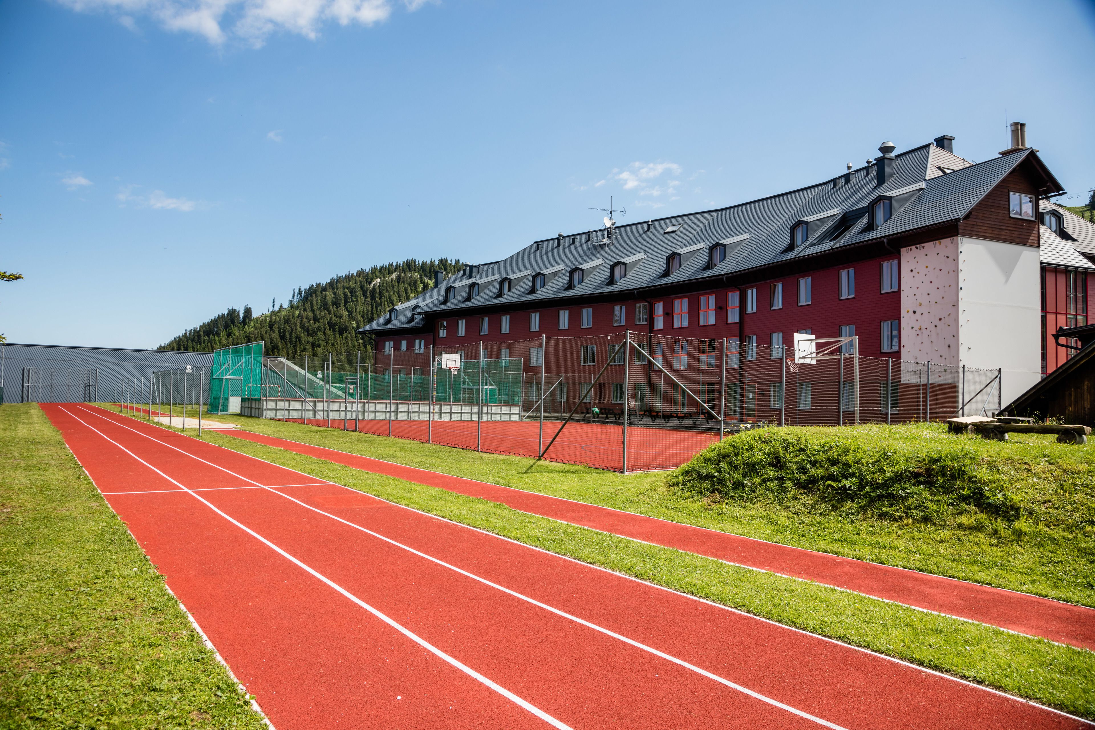Una pista de atletismo roja con un campo verde y un edificio rojo con numerosas ventanas.