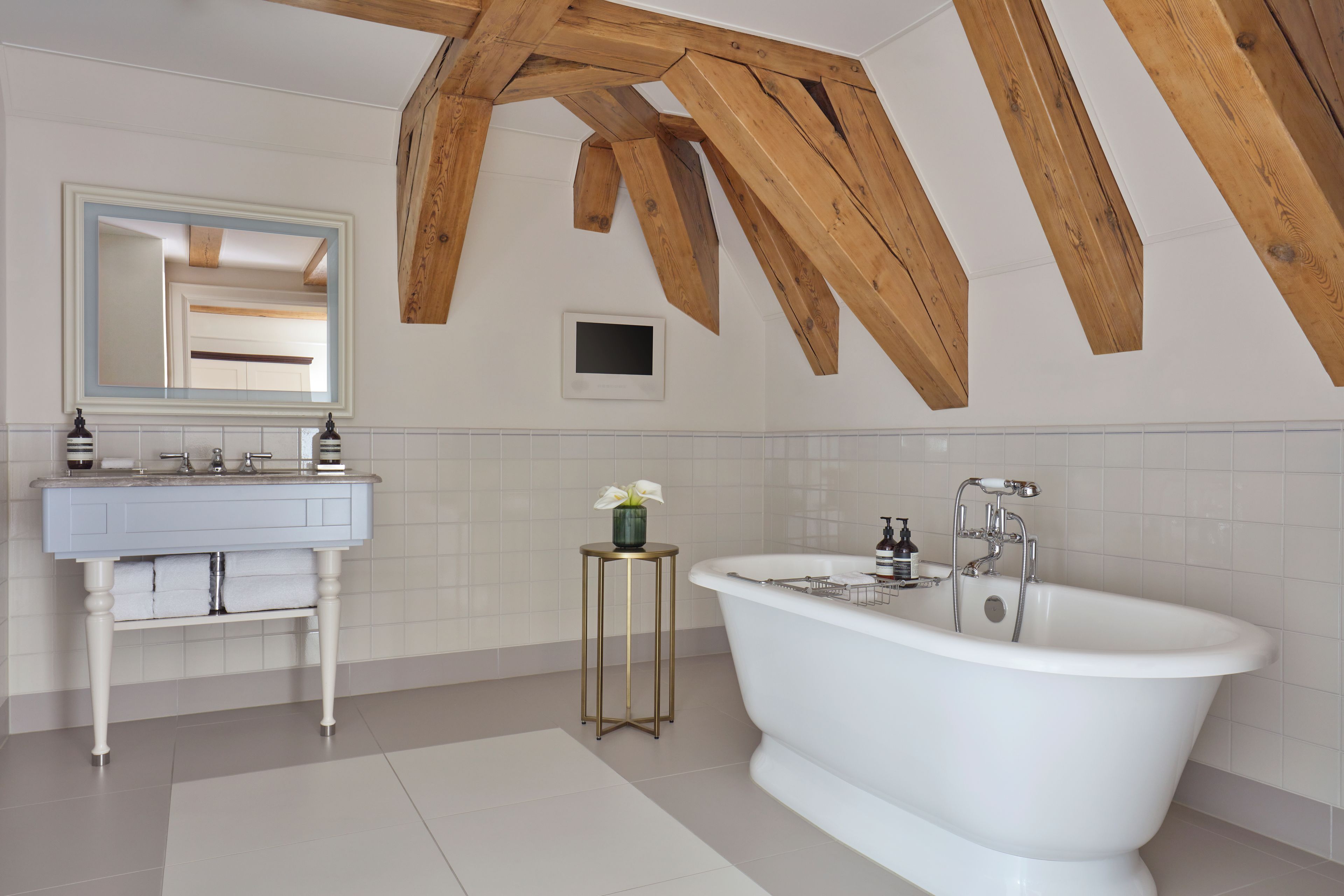 A bathroom with a freestanding bathtub, a vanity with a mirror, and a small table with a vase.