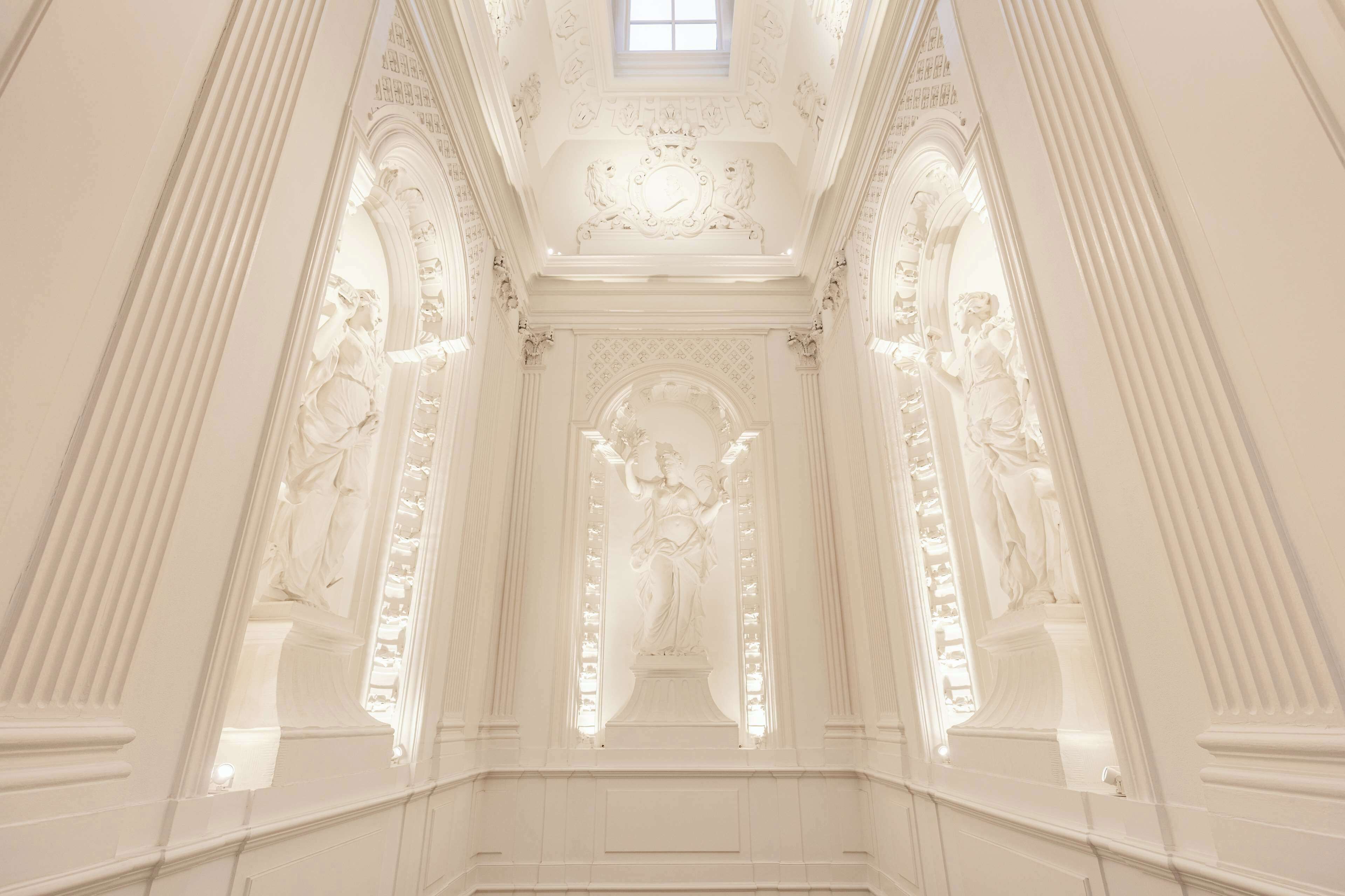 An ornate hallway with classical architecture, including columns and statues.