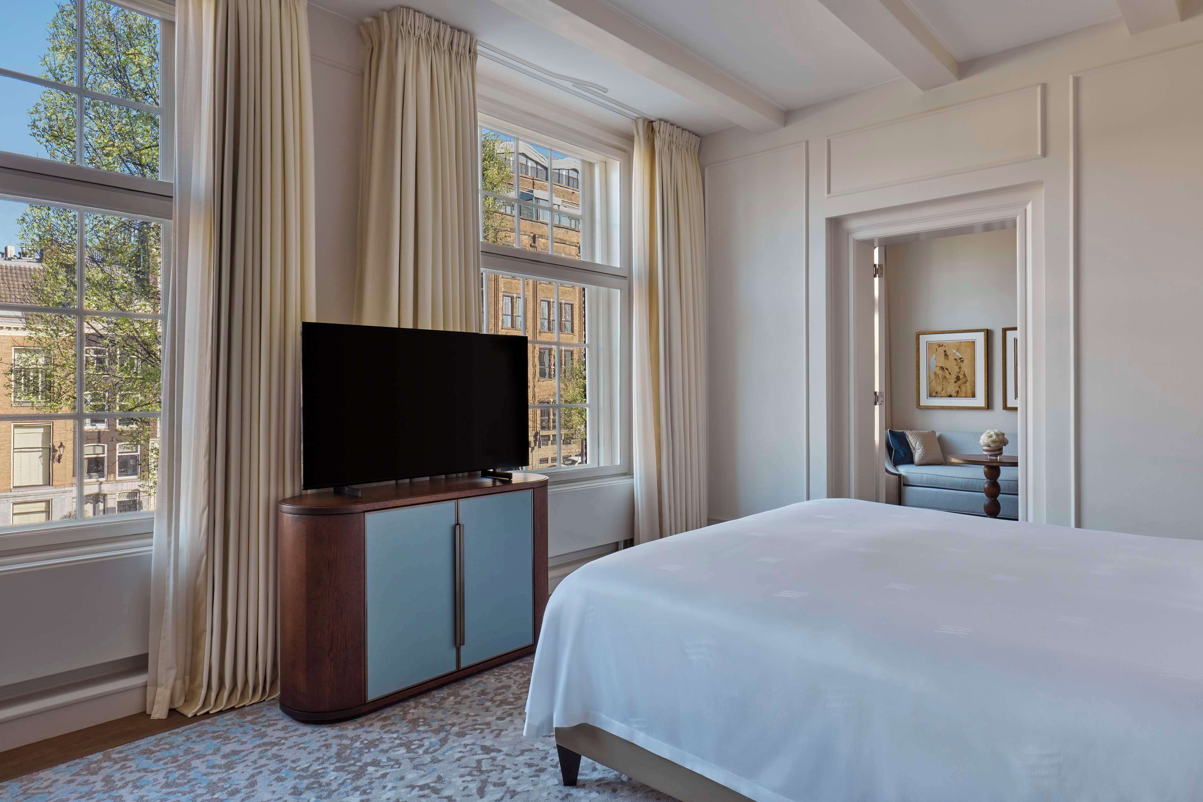 A hotel room with a large bed, a television on a cabinet, and a view of buildings through the window.