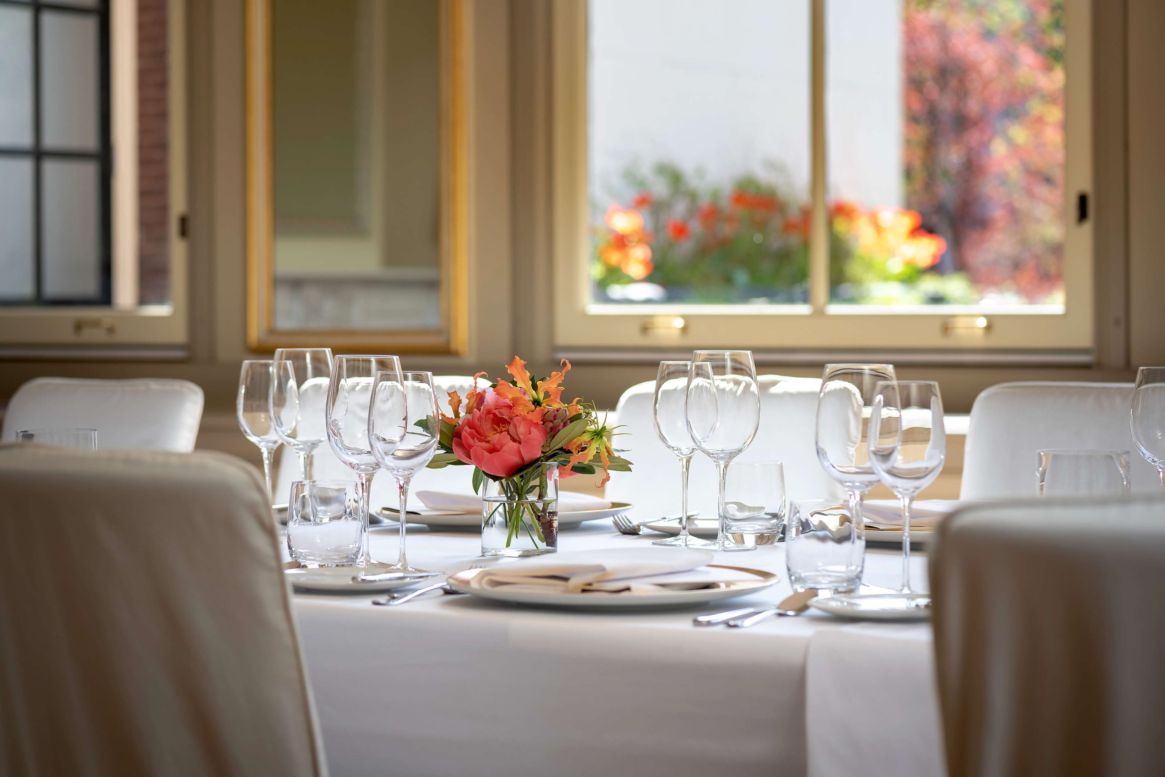 Une table à manger dressée pour un repas, avec de nombreux verres à vin, des assiettes et des couverts, et un vase rempli de fleurs placé au centre.