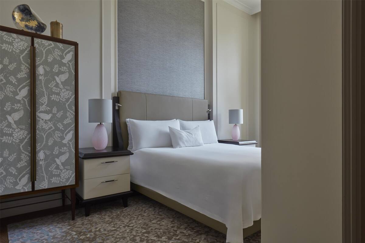 A hotel room with a large bed, two bedside tables, a wardrobe, and a grey headboard.