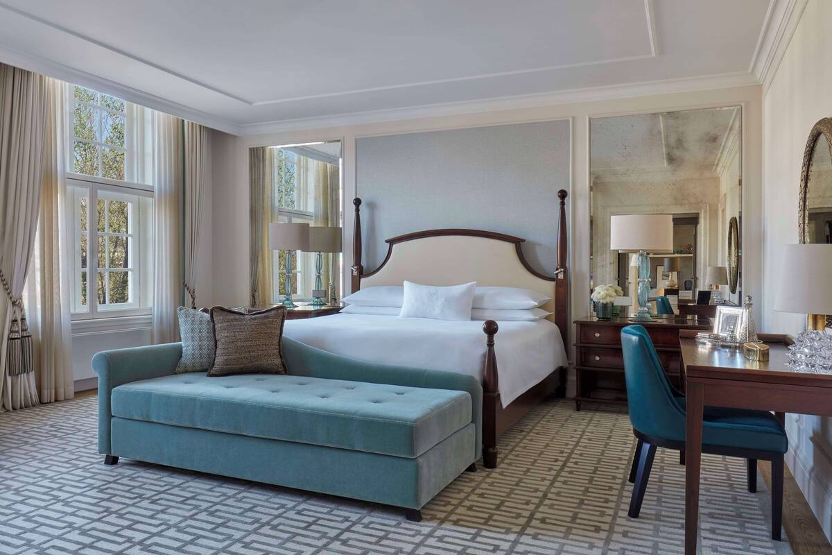 A spacious bedroom with a large bed, a matching bench, a desk, and a mirror.