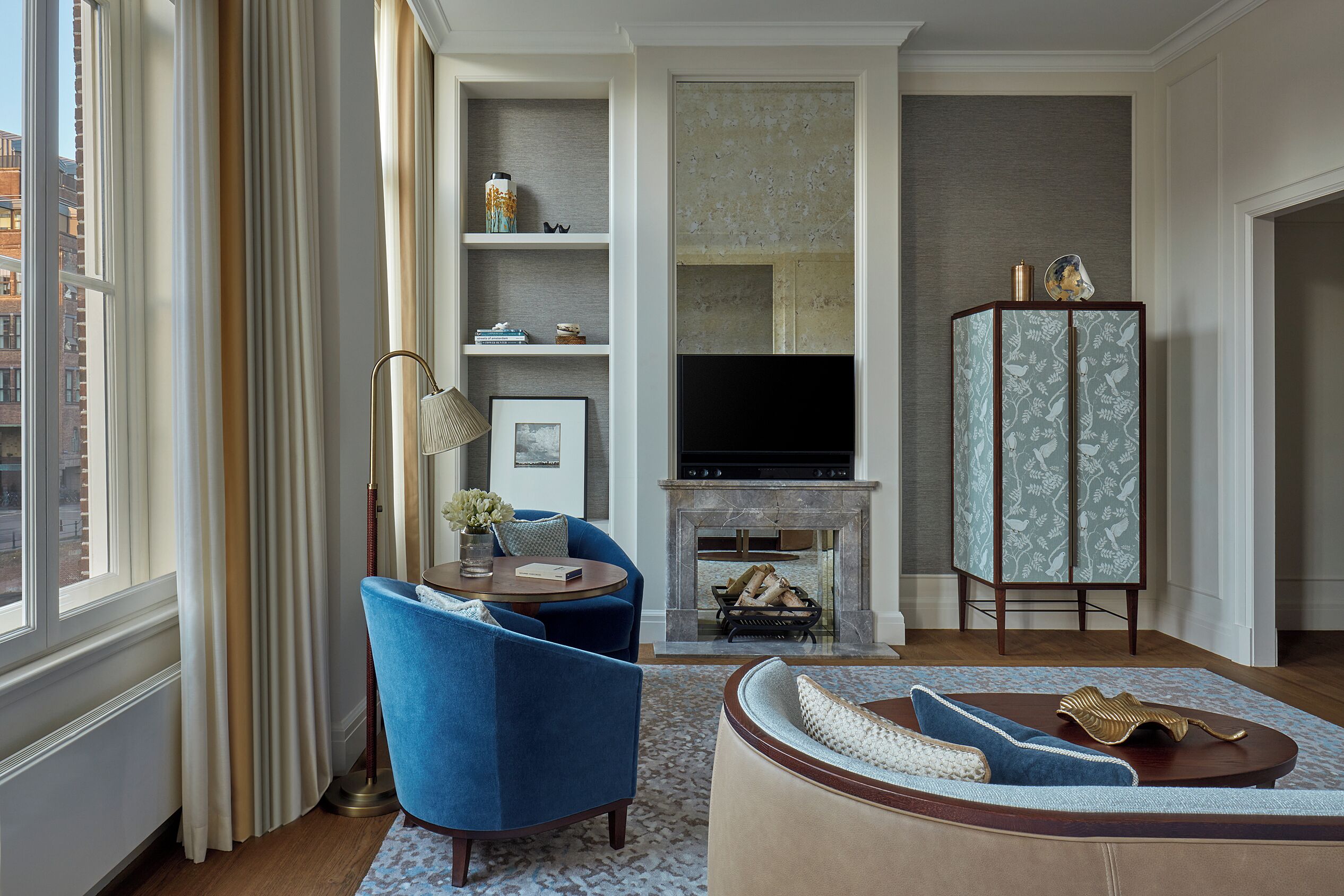 A living room with a fireplace, blue armchairs, a sofa, and a cabinet.