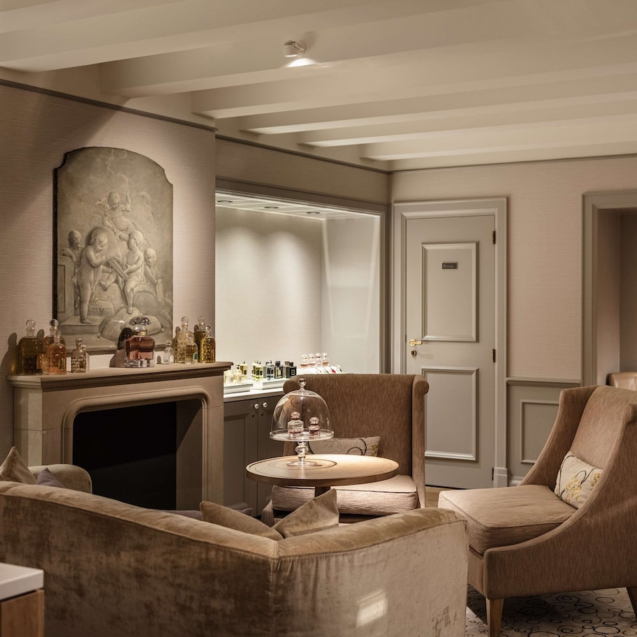 A luxurious living room with a fireplace, comfortable seating, and a display of perfume bottles.