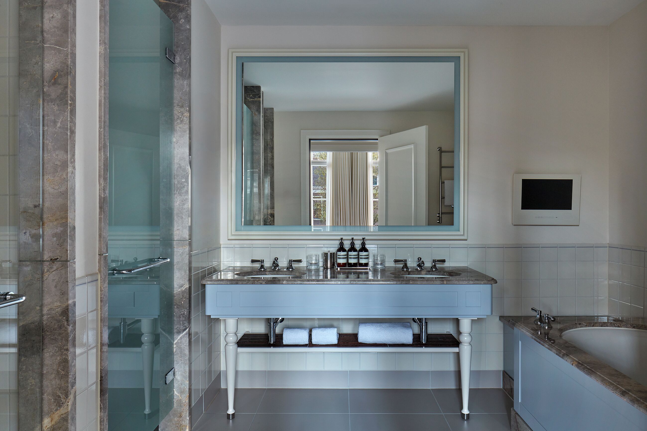 A modern bathroom with a marble shower, a large mirror, a double sink vanity, and a bathtub.