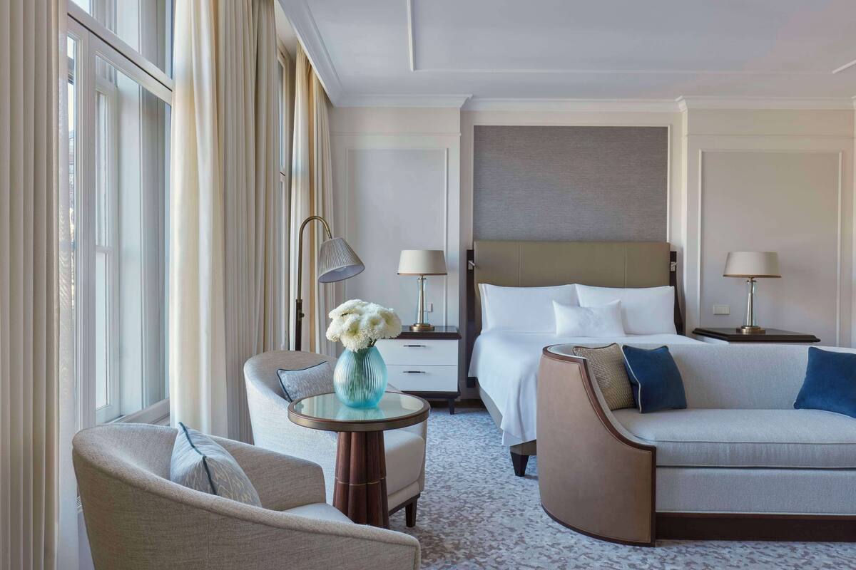 A hotel room with a bed, two bedside tables, a sofa, a chair, and a small table with a vase.