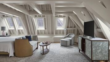 A modern loft bedroom with skylights, a bed, a sofa, a TV, and a side table.