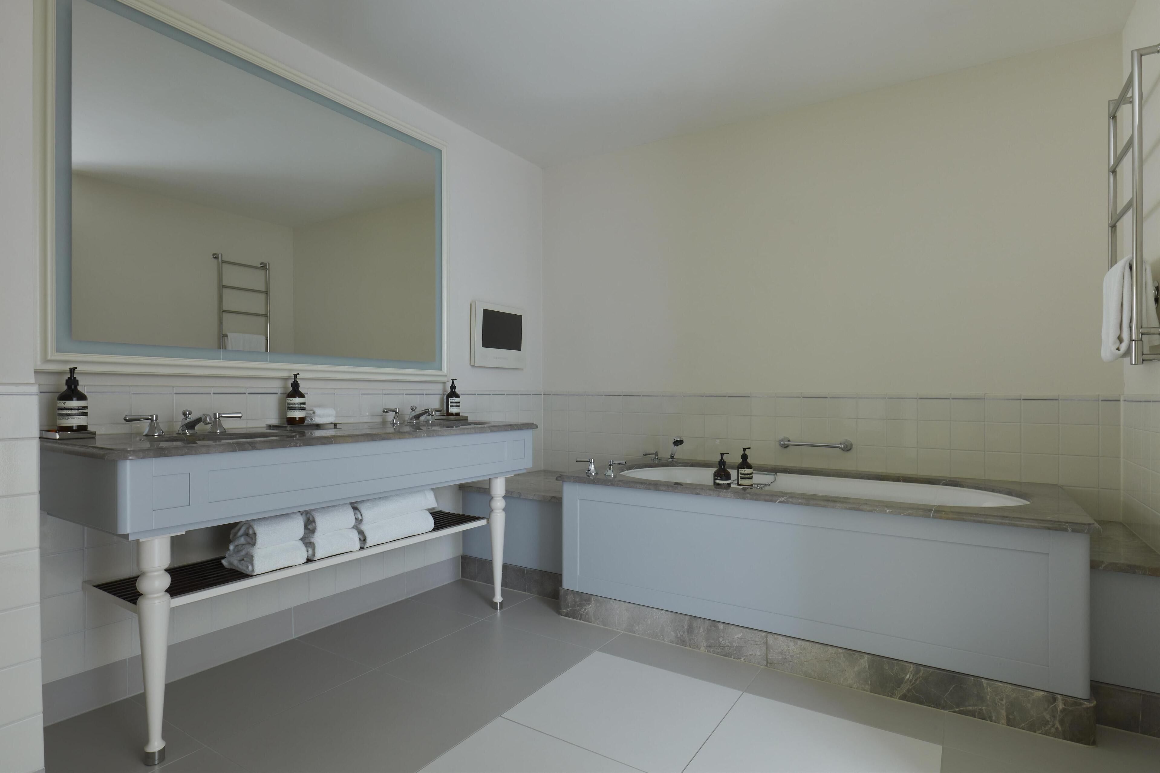 A modern bathroom with a double sink vanity, a large mirror, a bathtub, and a towel rack.