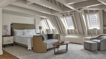 Una camera da letto moderna con un letto, un divano, una poltrona e un tavolino. La stanza ha travi a vista con lucernari e un tappeto decorato.