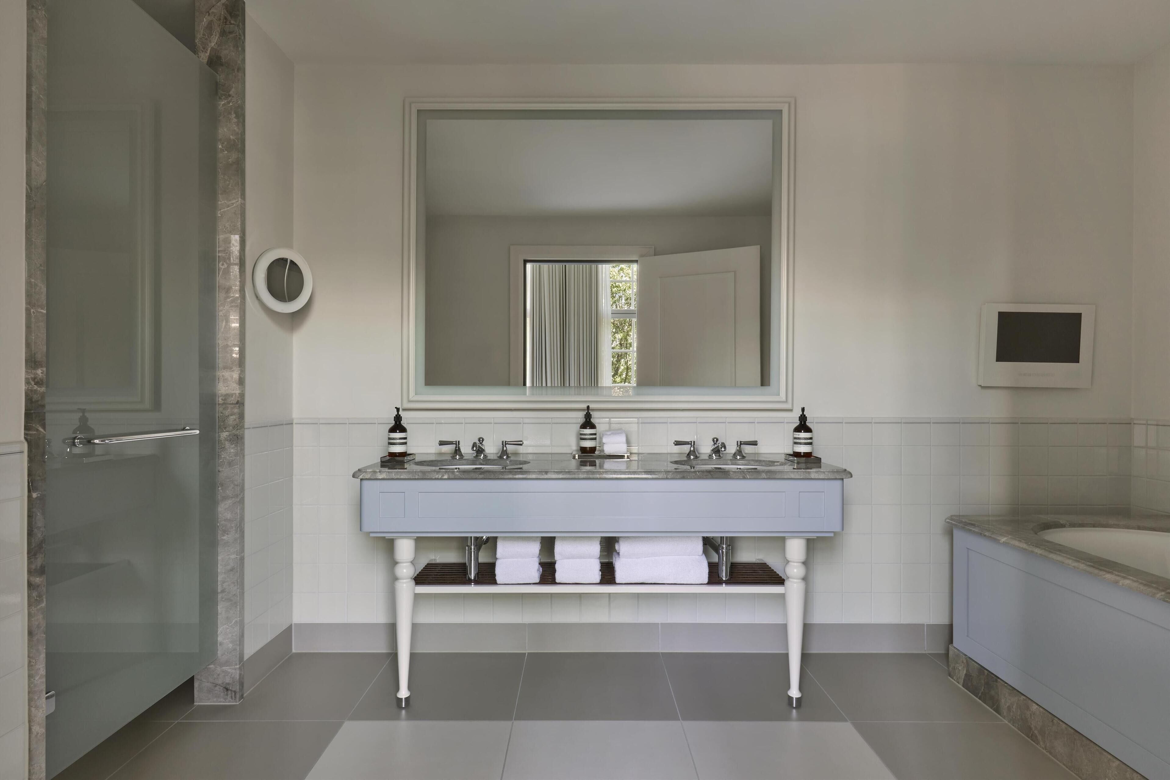 A modern bathroom with a double sink, a large mirror, a toilet, and a bathtub.