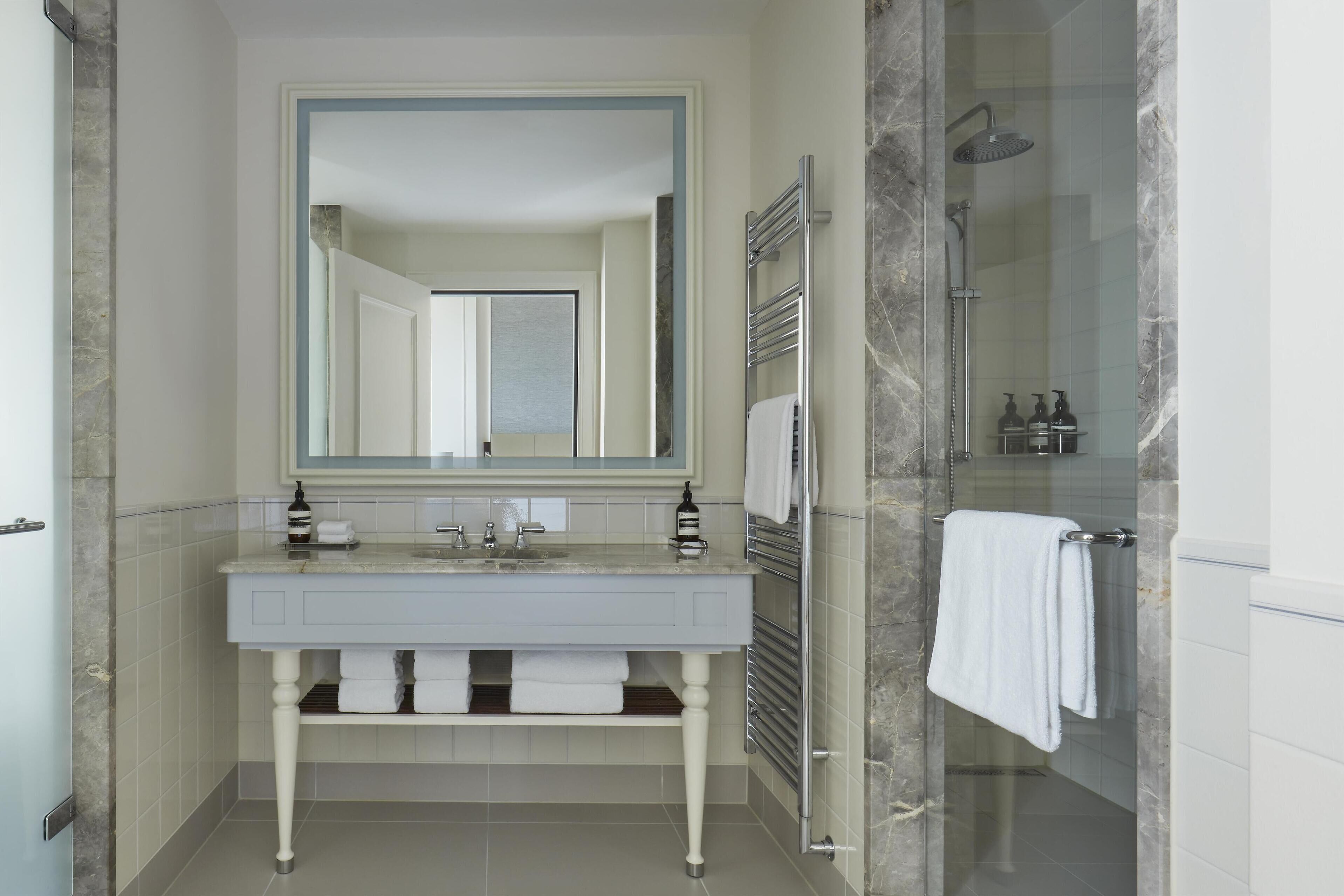 A modern bathroom with a white vanity, a large mirror, a glass shower enclosure, and a towel rack.