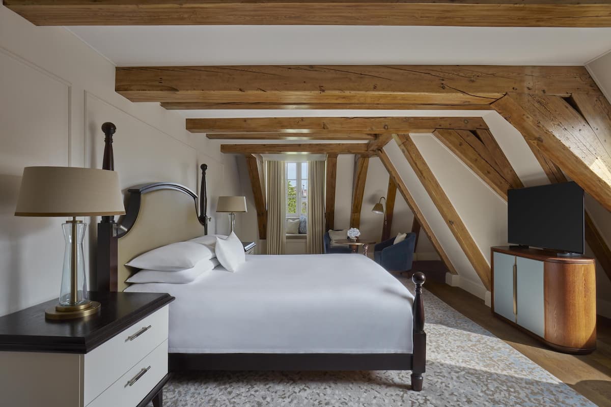 A bedroom with a large bed, wooden beams, a TV, and a desk with lamps.