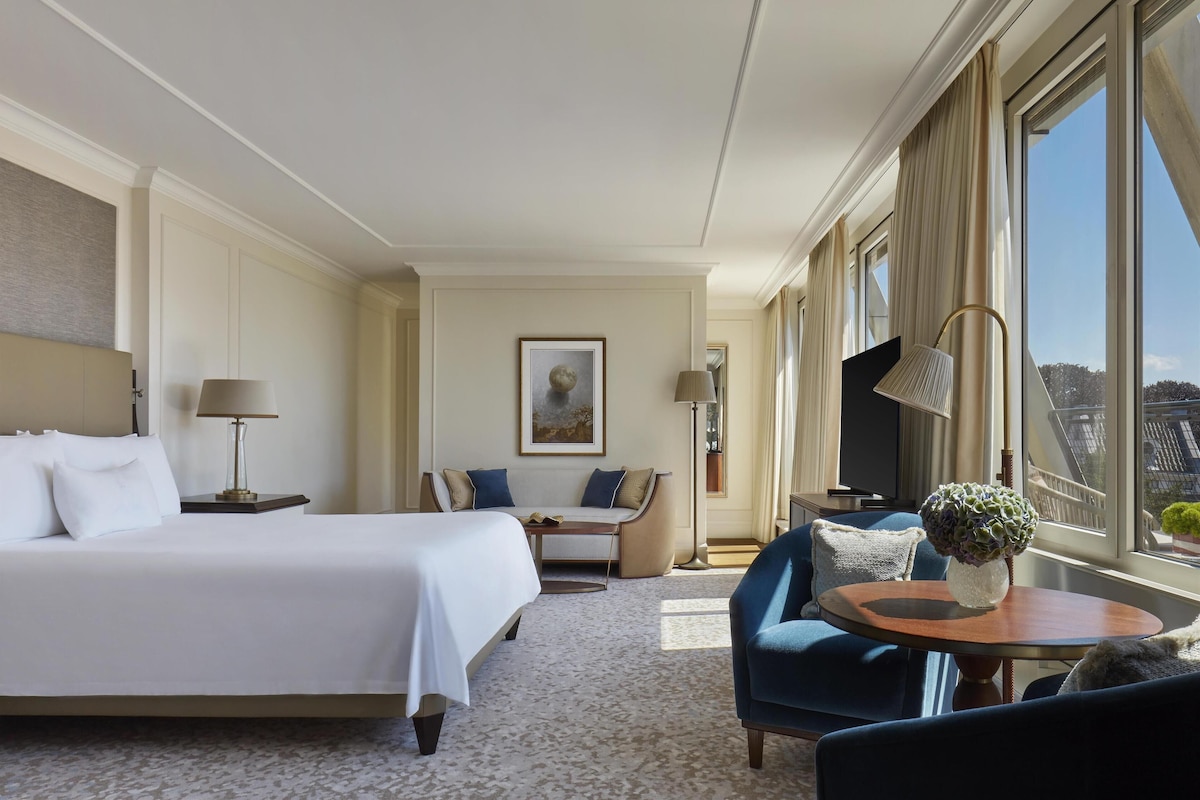 Habitación de hotel con una cama grande, un sofá, una mesa redonda con un florero y un televisor.