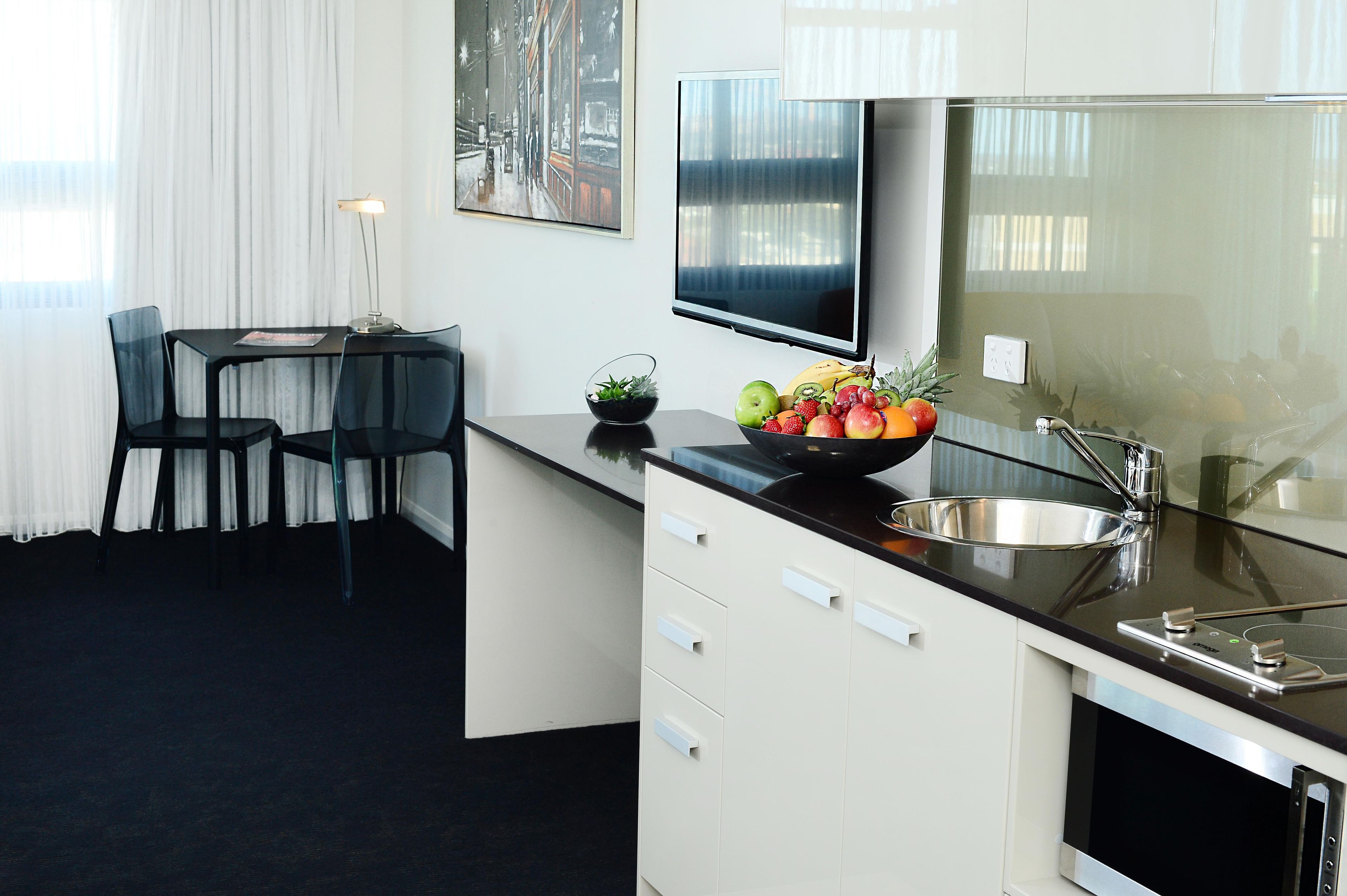 A modern kitchen with a black countertop, white cabinets, a stainless steel sink, and a fruit bowl.