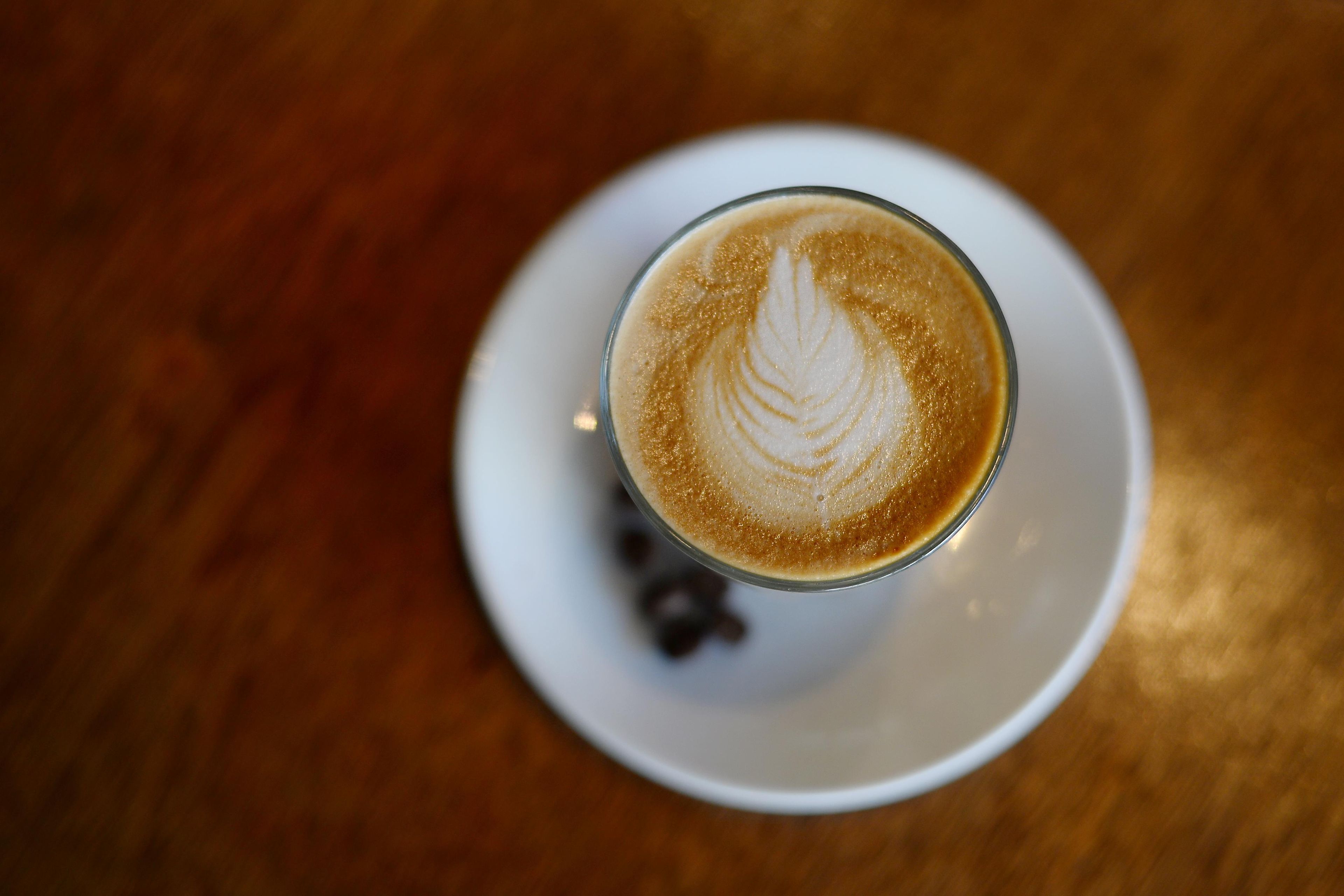 A glass of coffee with latte art on a white saucer.