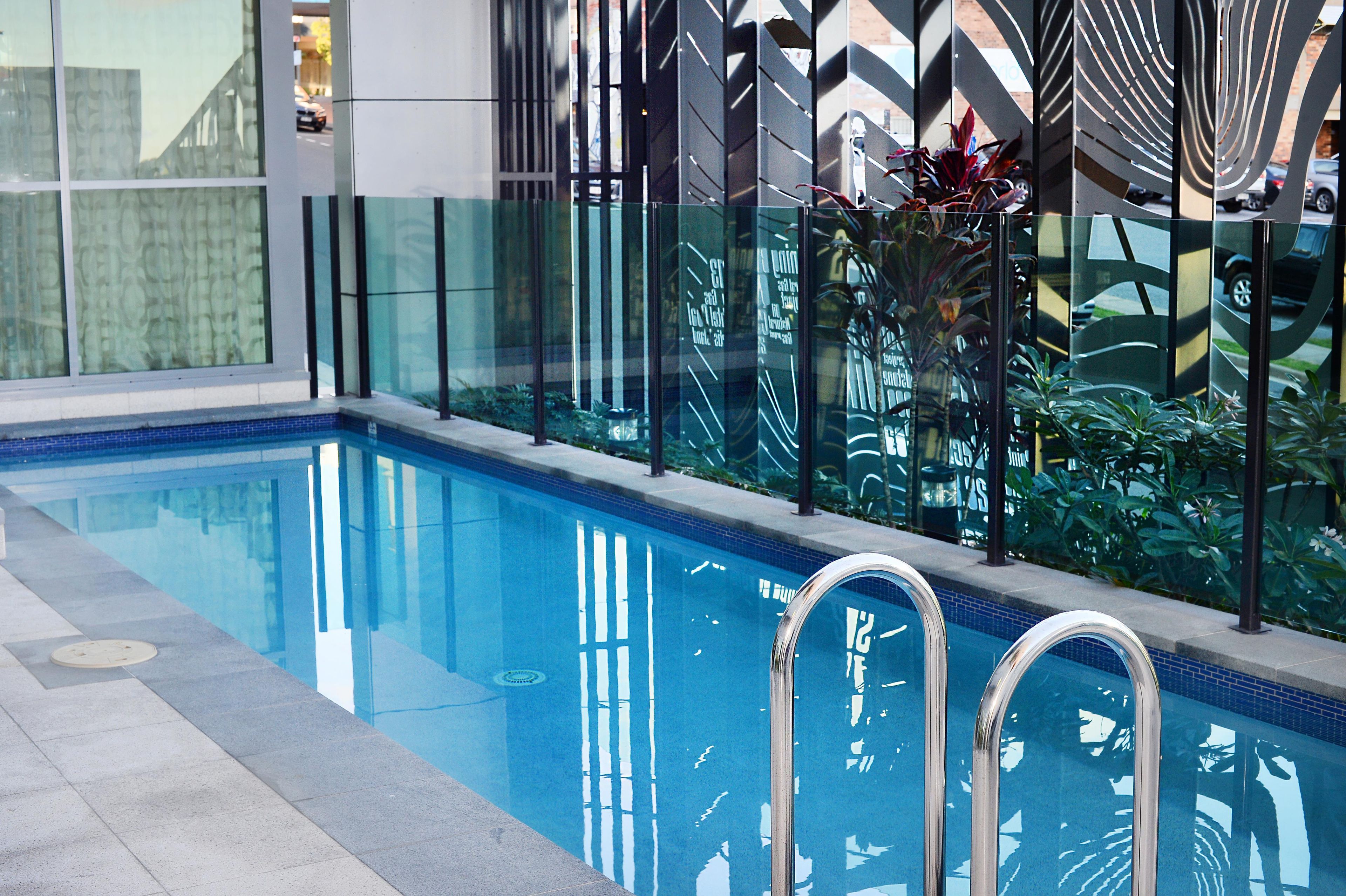 En swimmingpool med kristallklart blått vatten, omgiven av en modern glasvägg med vertikala linjer.
