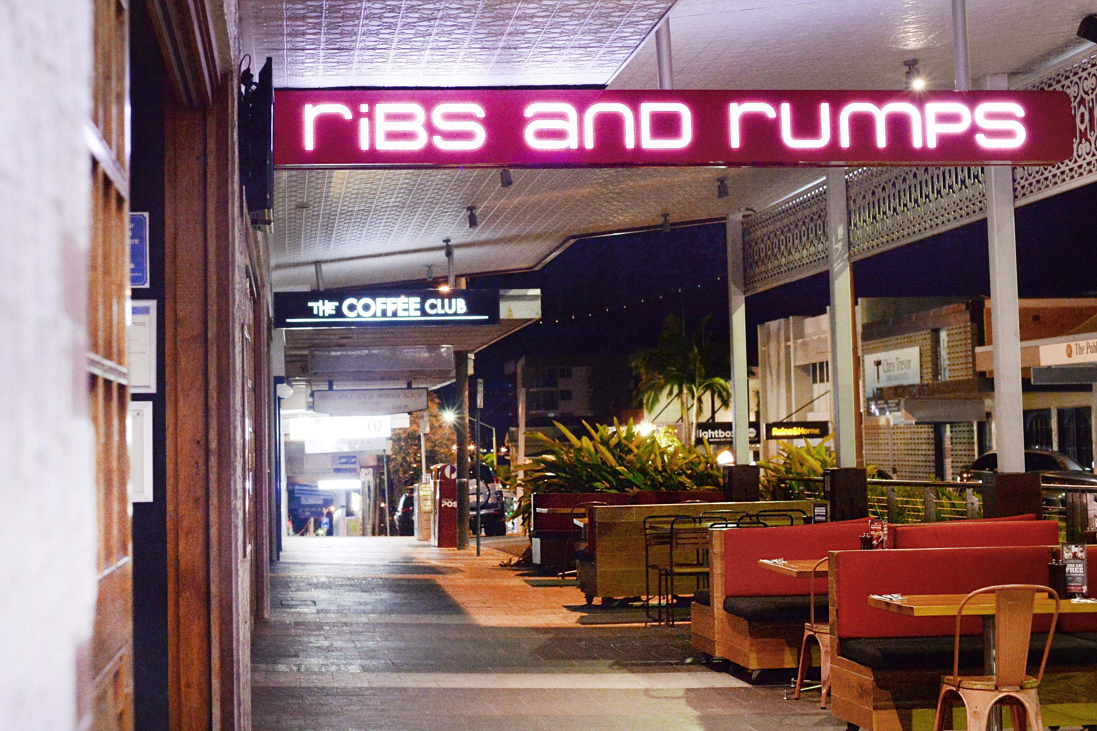 Ein Korridor mit Sitzbereichen und einem Neon-Schild mit der Aufschrift 'RIBS AND RUMPS'.