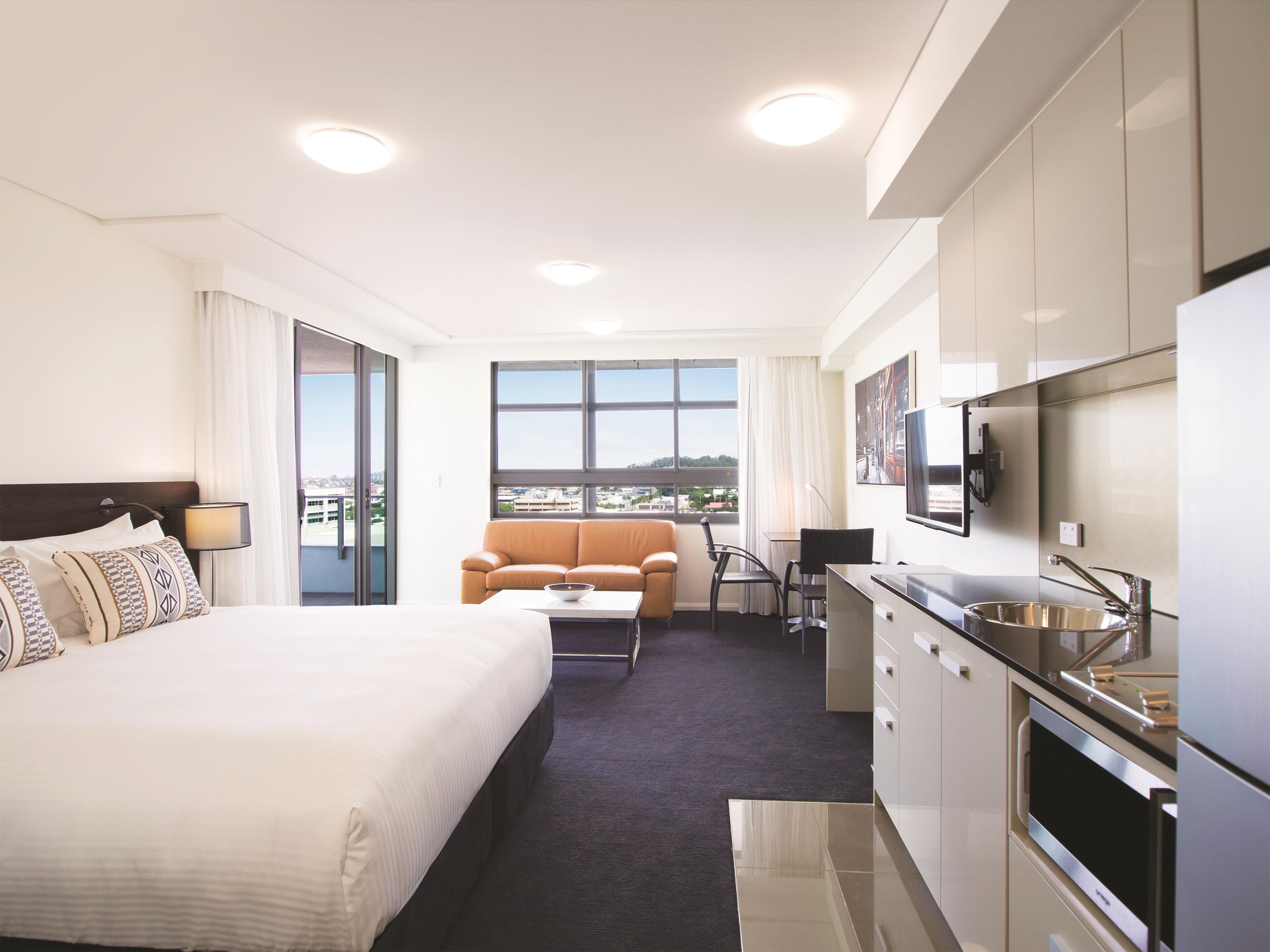 Una habitación de hotel con cama, sofá, escritorio, televisor y una zona de cocina.