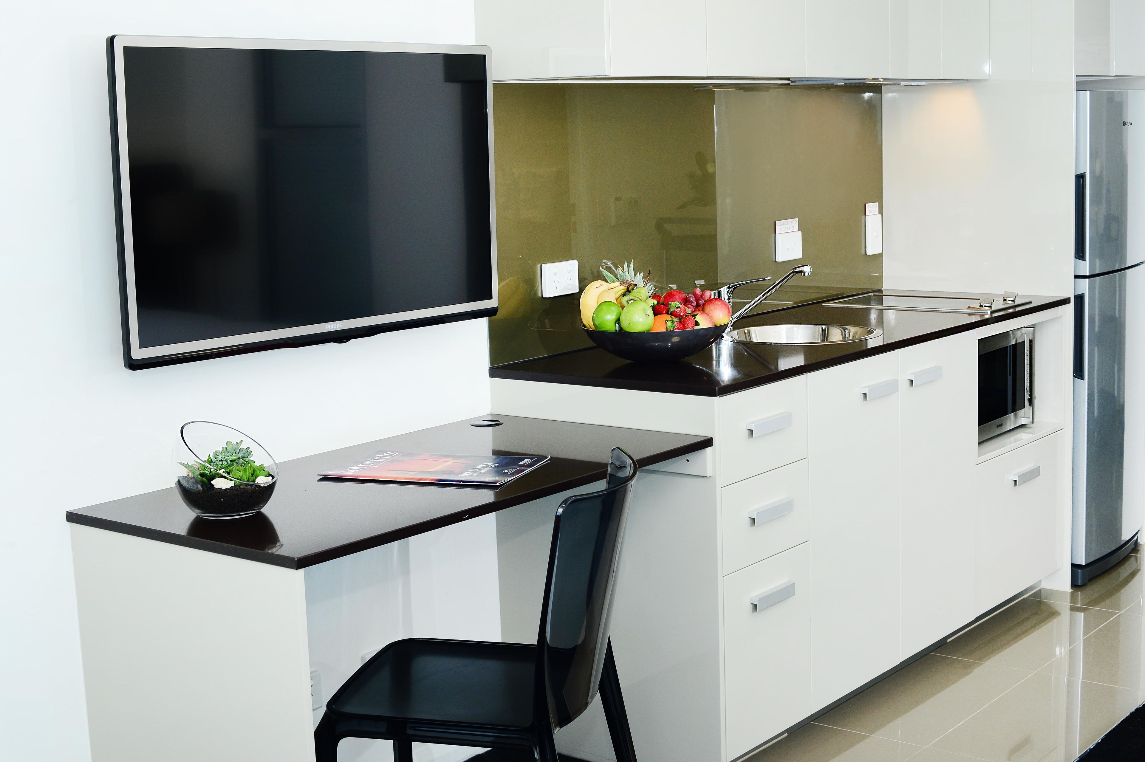 Cocina moderna con televisor de pantalla plana, frutero, pileta y refrigerador.