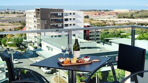 Un balcon avec une table dressée pour un repas, une bouteille de vin et une vue sur le paysage urbain et la mer.