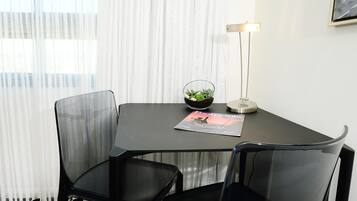 A modern office space with a glass table, two black chairs, a small potted plant, a lamp, and a magazine on the table.