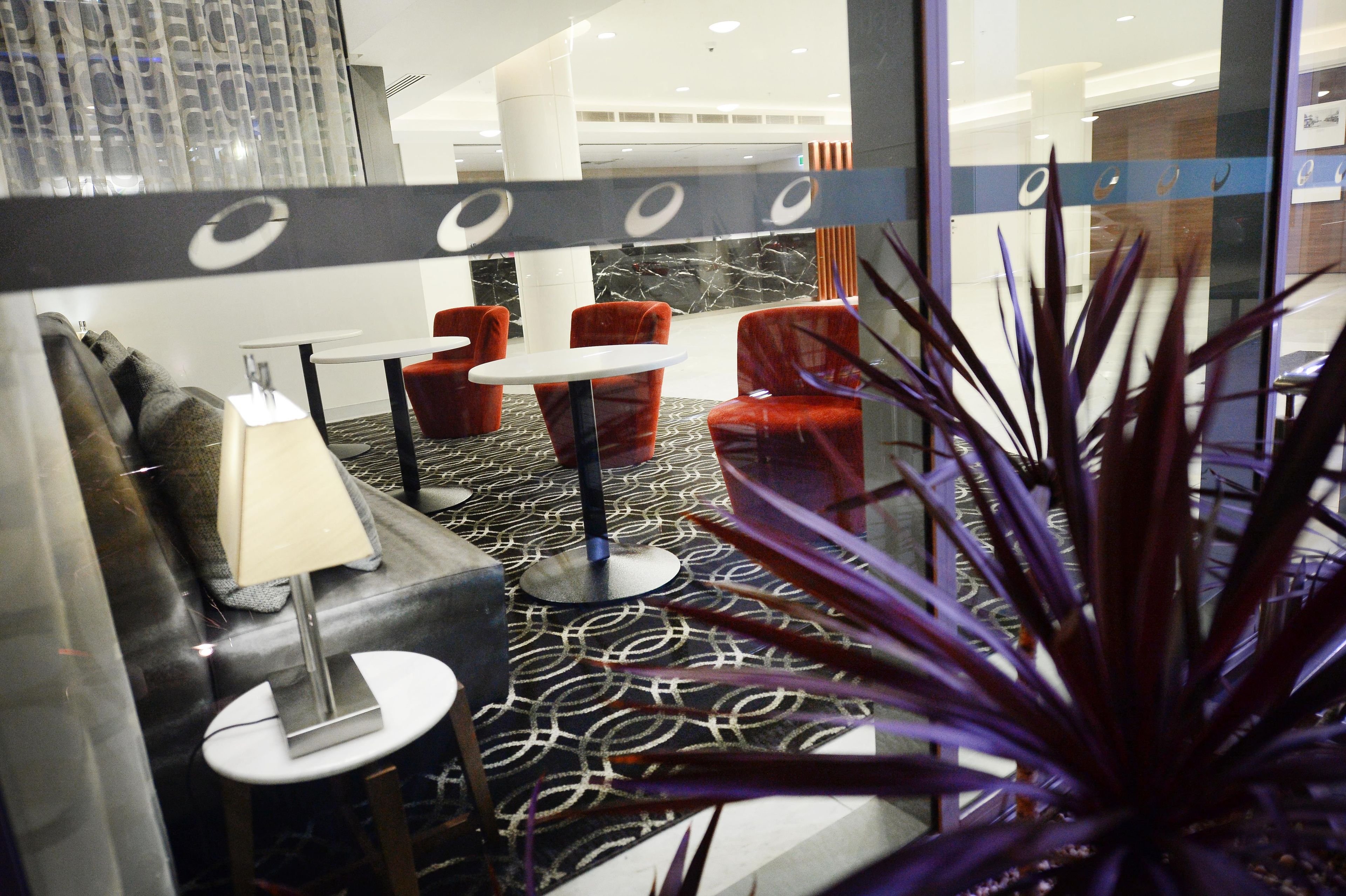 A hotel lobby with a patterned carpet, red chairs, a white table, and a lamp.