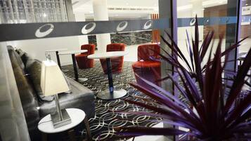 A hotel lobby with a patterned carpet, red chairs, a white table, and a lamp.