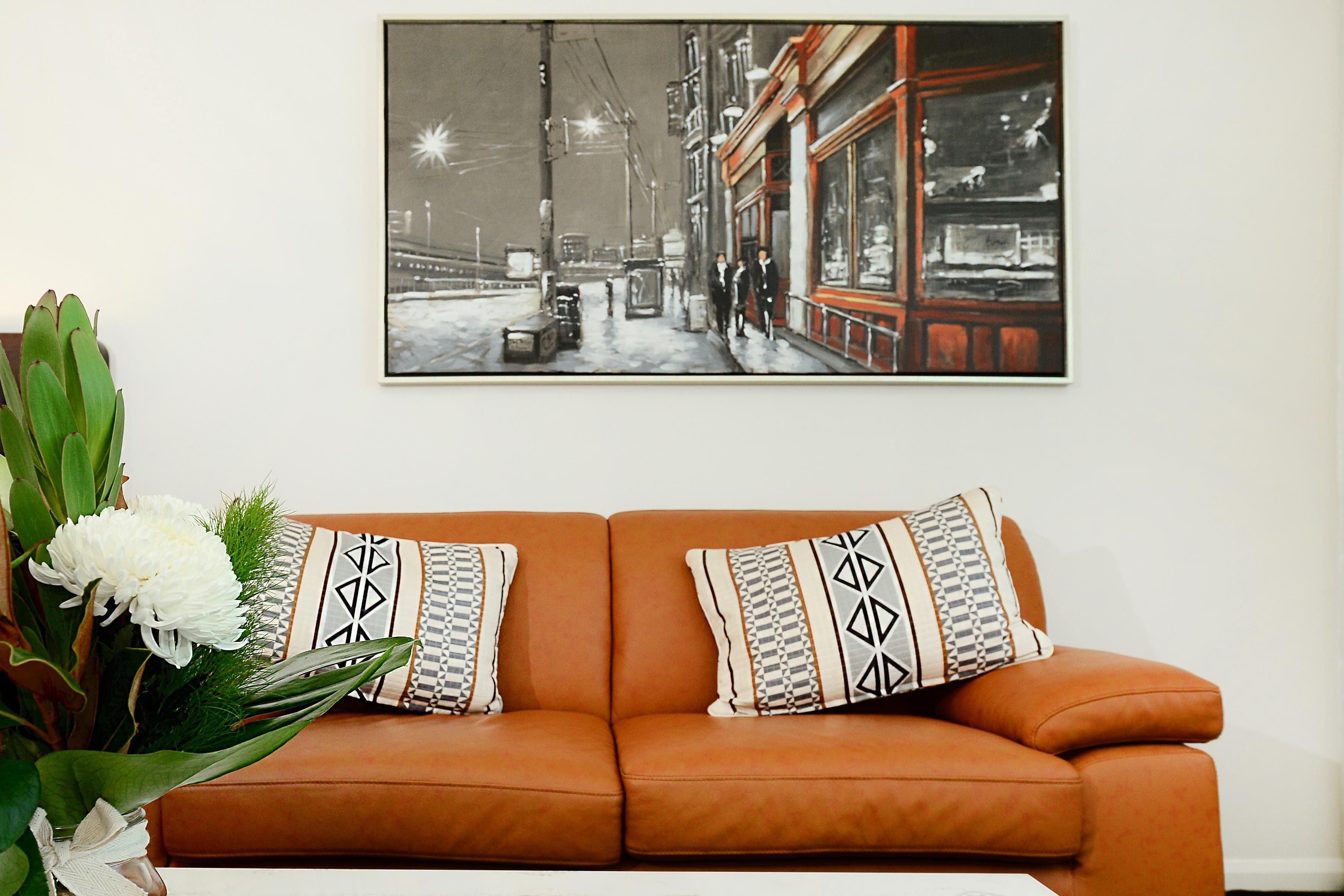 Une pièce avec un canapé en cuir marron, deux coussins à motifs et une photographie en noir et blanc encadrée accrochée au mur.