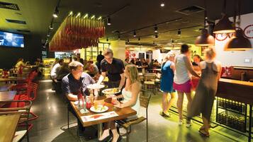 A restaurant with multiple dining tables and chairs, a bar area, and a television screen on the wall.