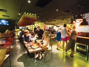 Een restaurant met meerdere eettafels en stoelen, een bar en een televisie aan de muur.