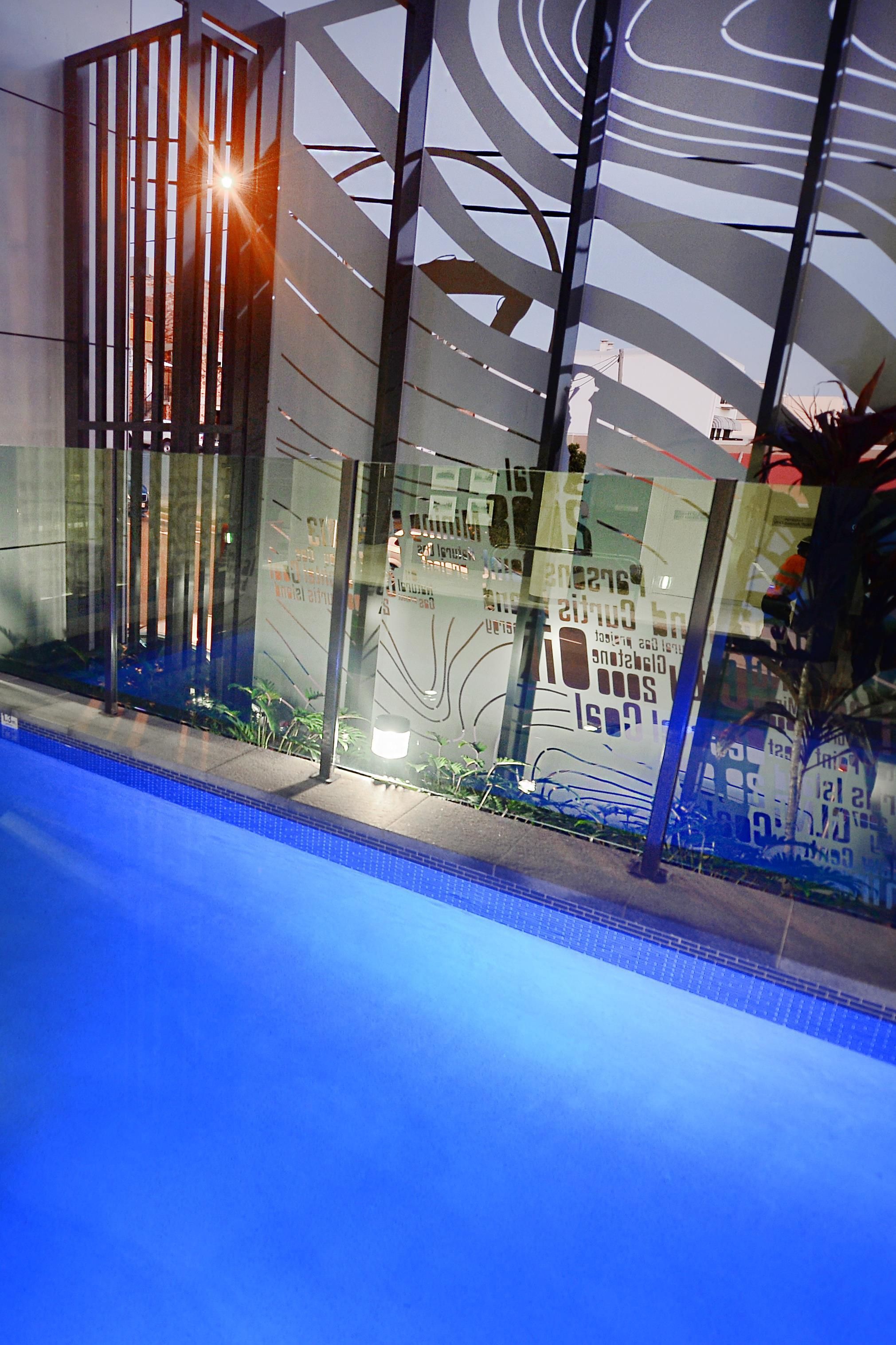 A modern building with a glass facade, a pool area, and a reflection of the sky.