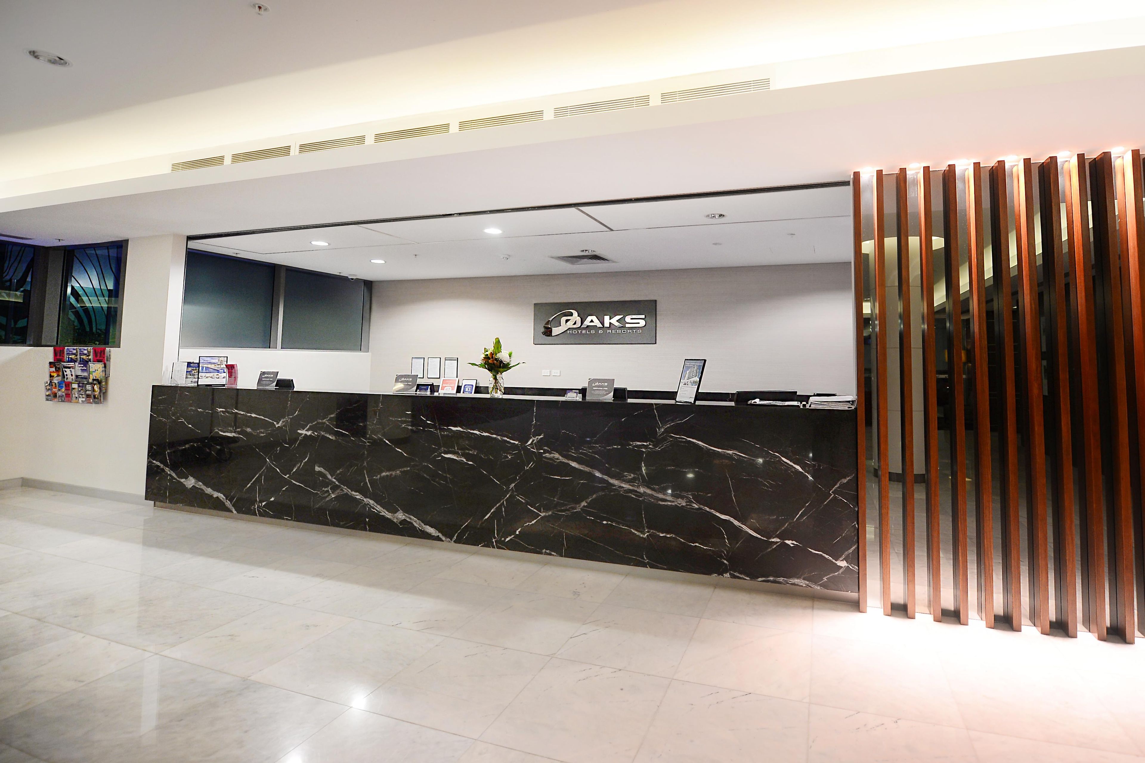 En receptionsdisk med sort marmortop, et skilt med 'OAKS Hotels & Resorts', og et moderne, minimalistisk design.