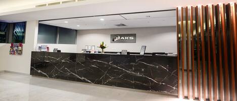 Un mostrador de recepción con encimera de mármol negro, un cartel de 'OAKS Hotels & Resorts' y un diseño moderno y minimalista.