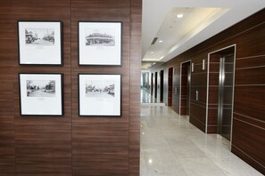 Un pasillo con fotografías blanco y negro enmarcadas en la pared, un ascensor moderno y un piso de mármol pulido.