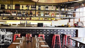 Un bar avec des tables en bois et des tabourets rouges, des étagères remplies de bouteilles et un plafond voûté.