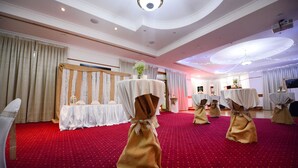 Una habitación con alfombra roja, cortinas blancas y mesas con manteles blancos y fajones dorados.