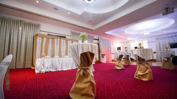 A room with a red carpet, white drapery, and tables with white tablecloths and gold sashes.
