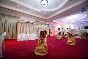 Una habitación con alfombra roja, cortinas blancas y mesas con manteles blancos y fajones dorados.