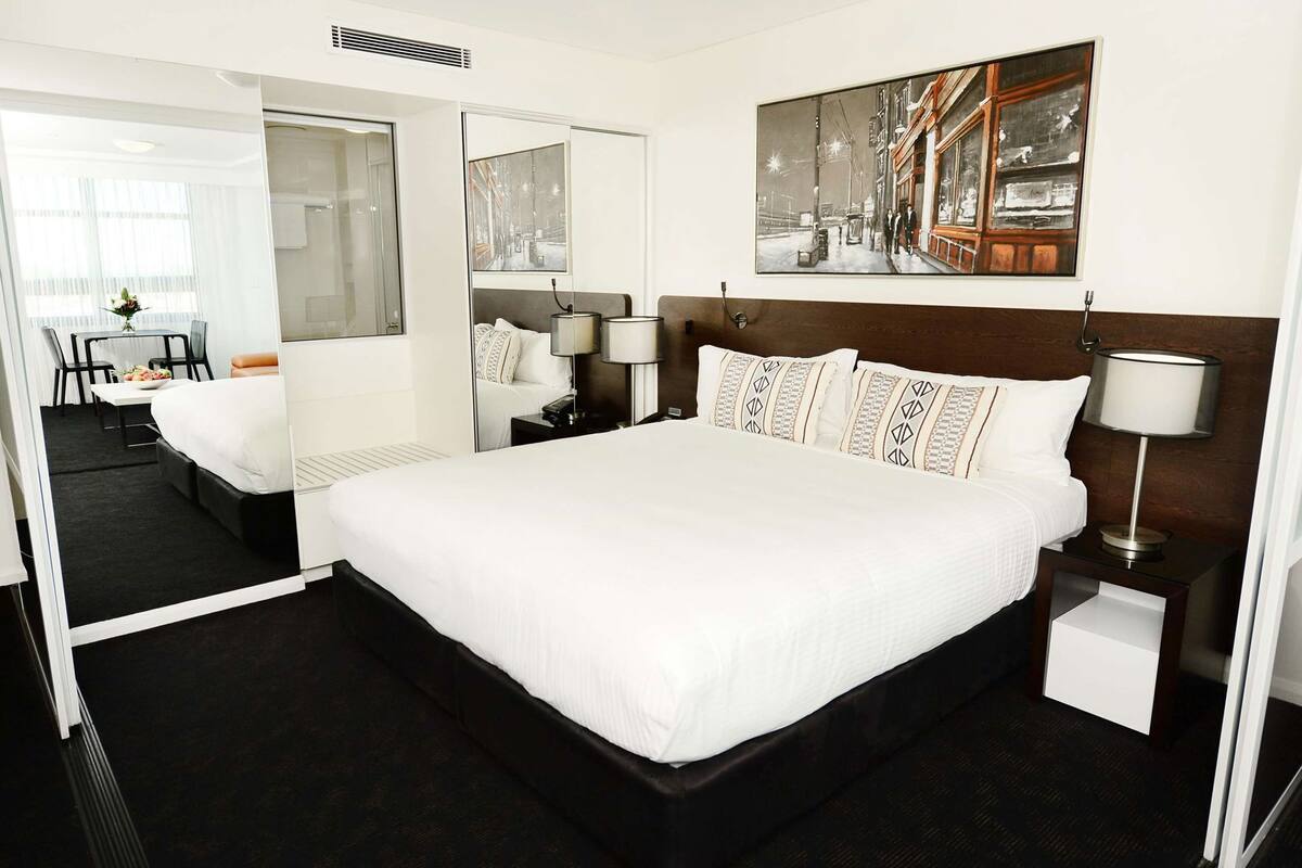 Een hotelkamer met een groot bed, een nachtkastje met een lamp, een spiegel en een schilderij aan de muur.