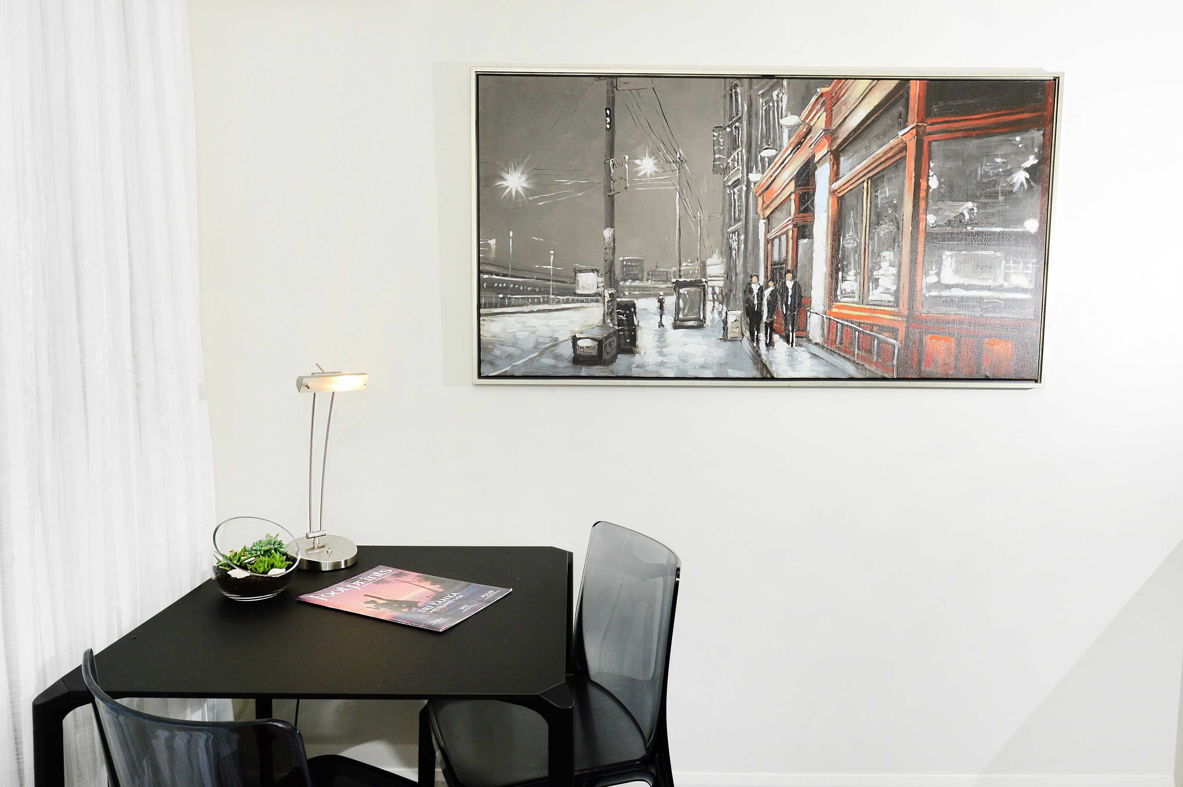 A dining area with a table, chairs, a lamp, a small plant, and a framed picture on the wall.