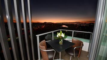 A balcony with a table and chairs, overlooking a cityscape at dusk.