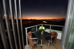 Un balcon avec une table et des chaises, donnant sur une vue panoramique de la ville au crépuscule.