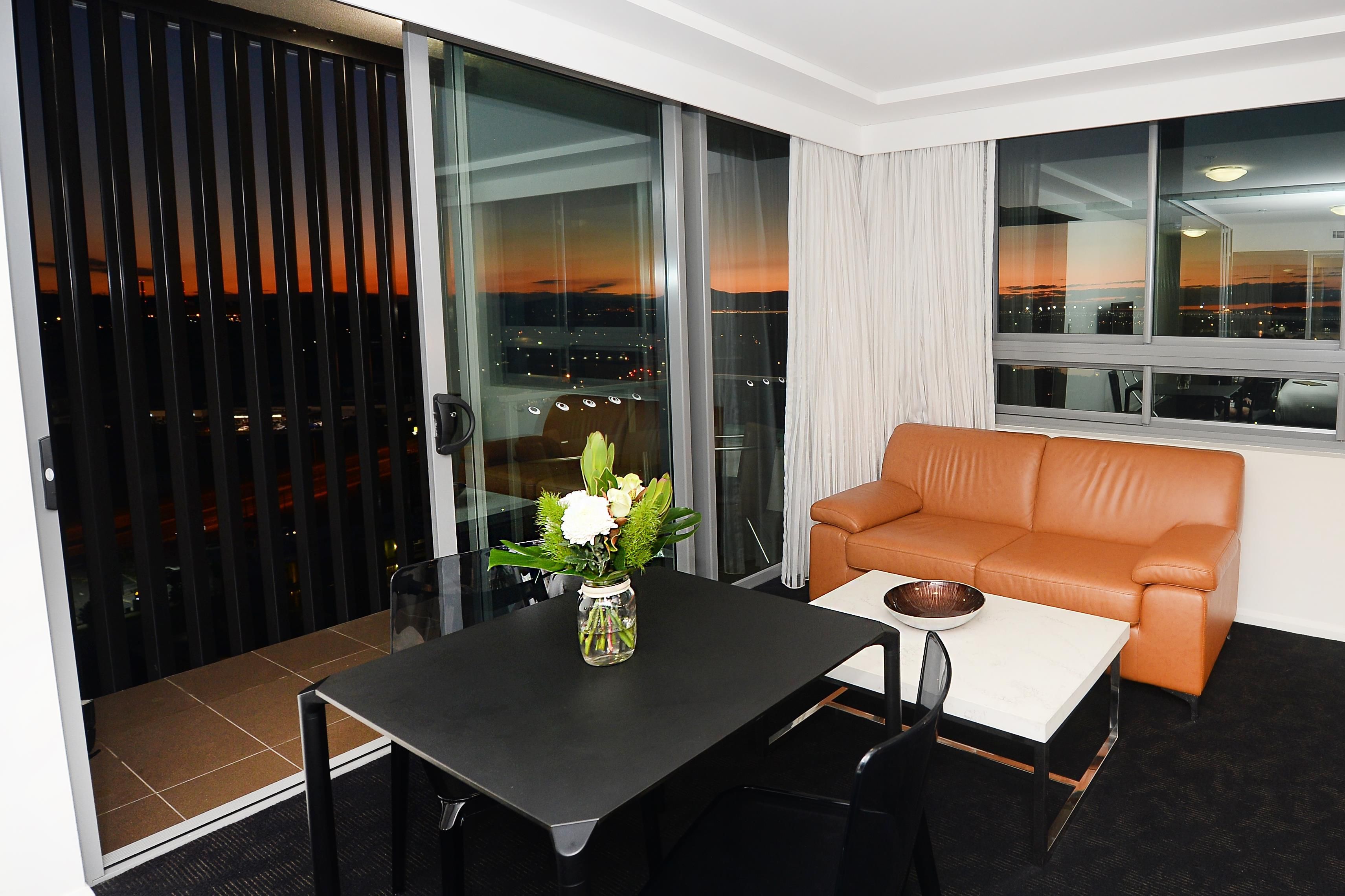 Una habitación de hotel moderna con una puerta de cristal, un sofá, una mesita y un florero con flores.