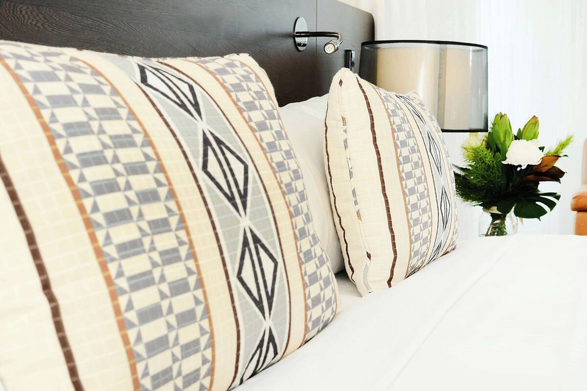 Una cama bien hecha con almohadones estampados y una mesita de noche con lámpara.
