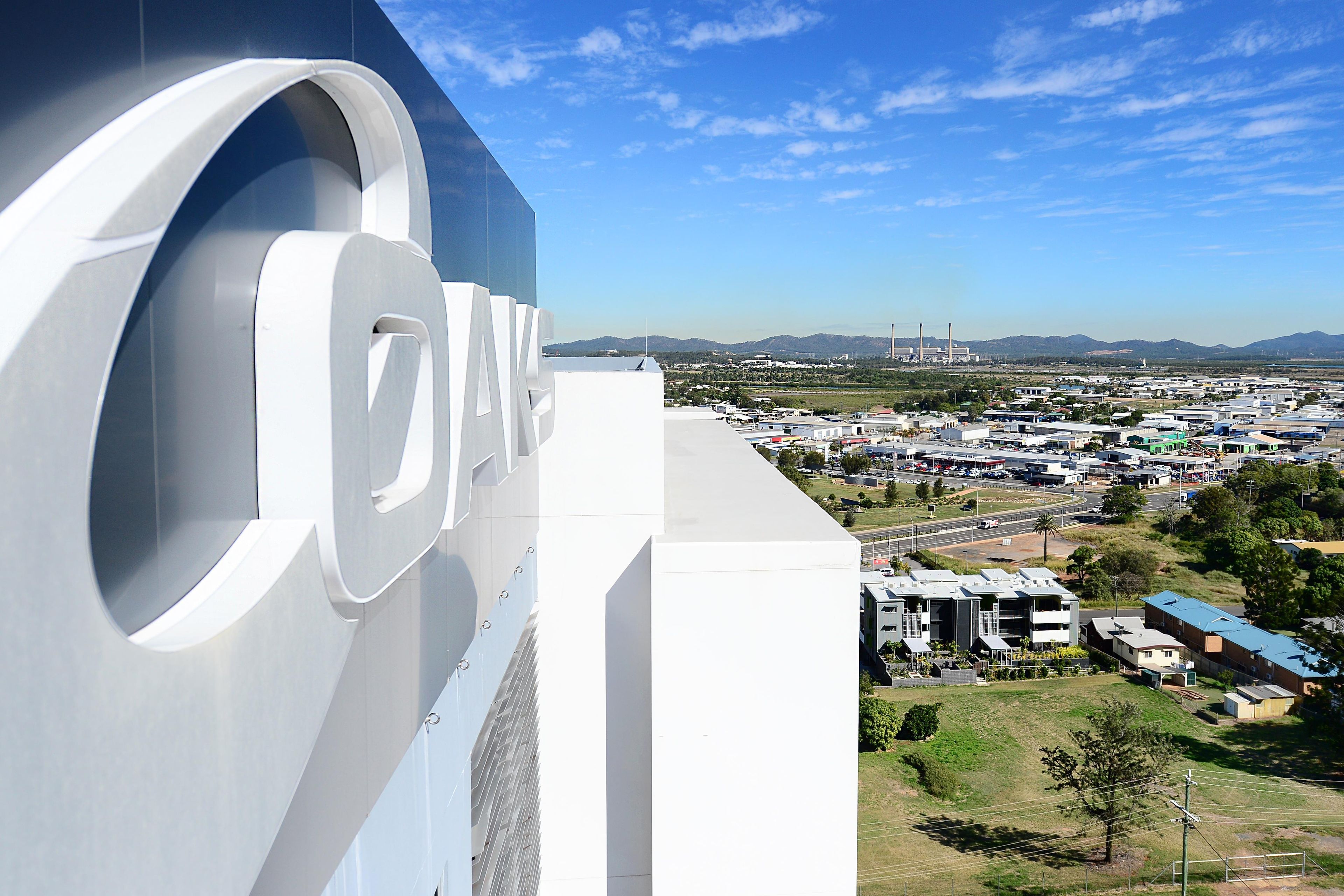 A large building with a prominent circular logo and a view of a cityscape with industrial buildings in the distance.