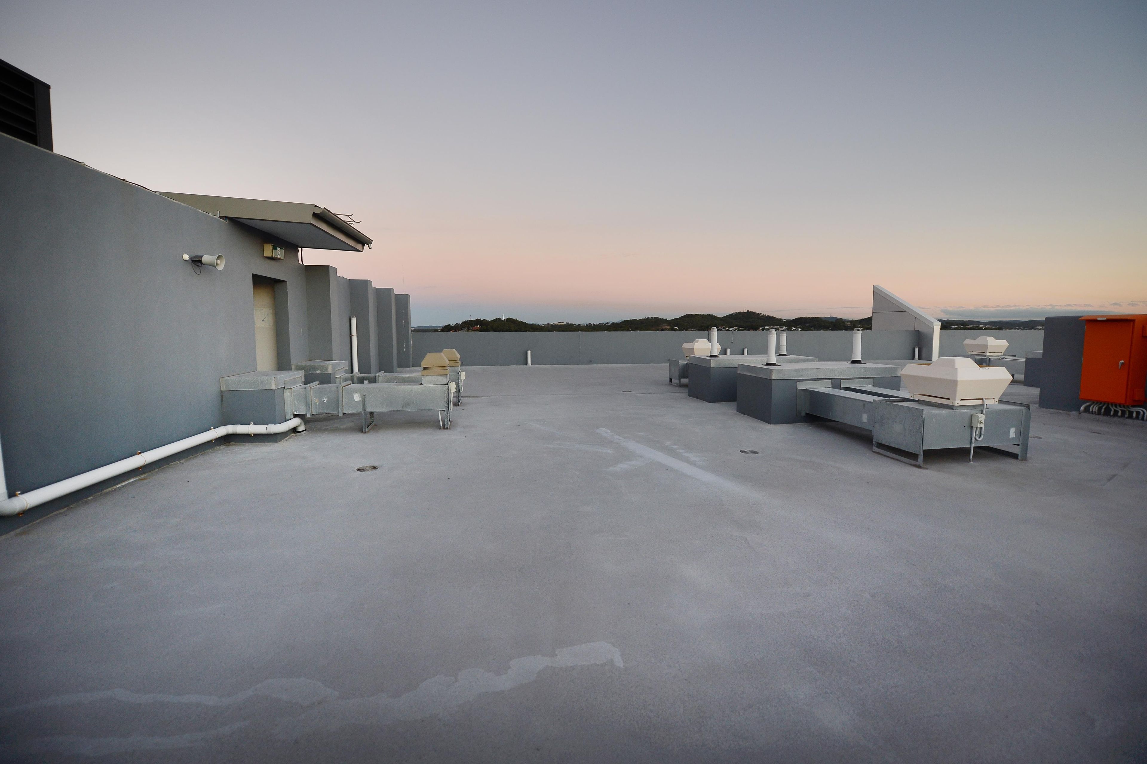 A rooftop terrace with a flat concrete floor, several white and grey structures, and a distant view of a hilly landscape.