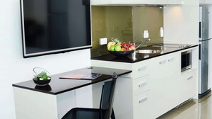 Una cocina moderna con una televisión de pantalla plana, un cuenco de fruta y una silla negra.