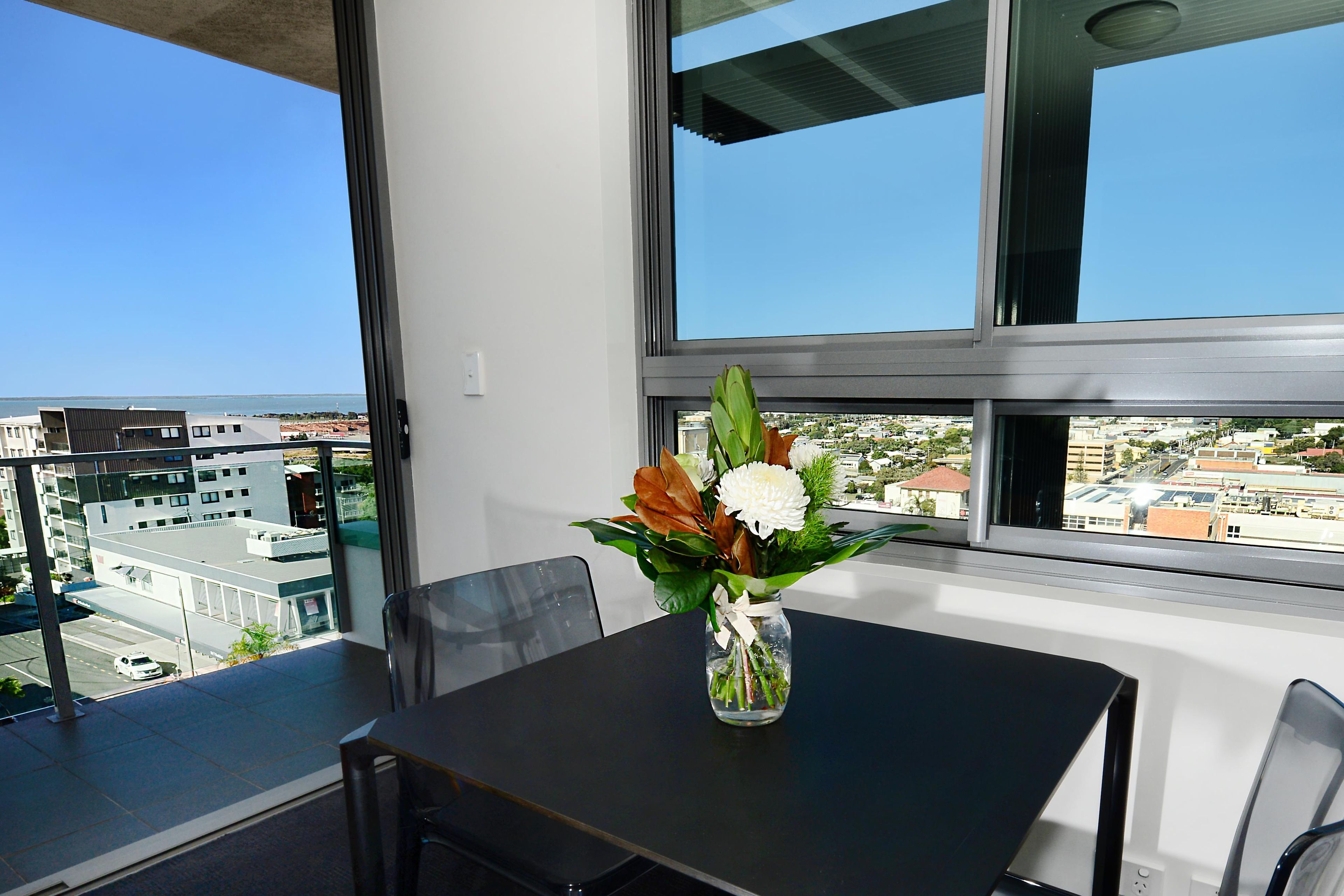 Un balcón con una mesa y sillas, un jarrón con flores y vistas a la ciudad.